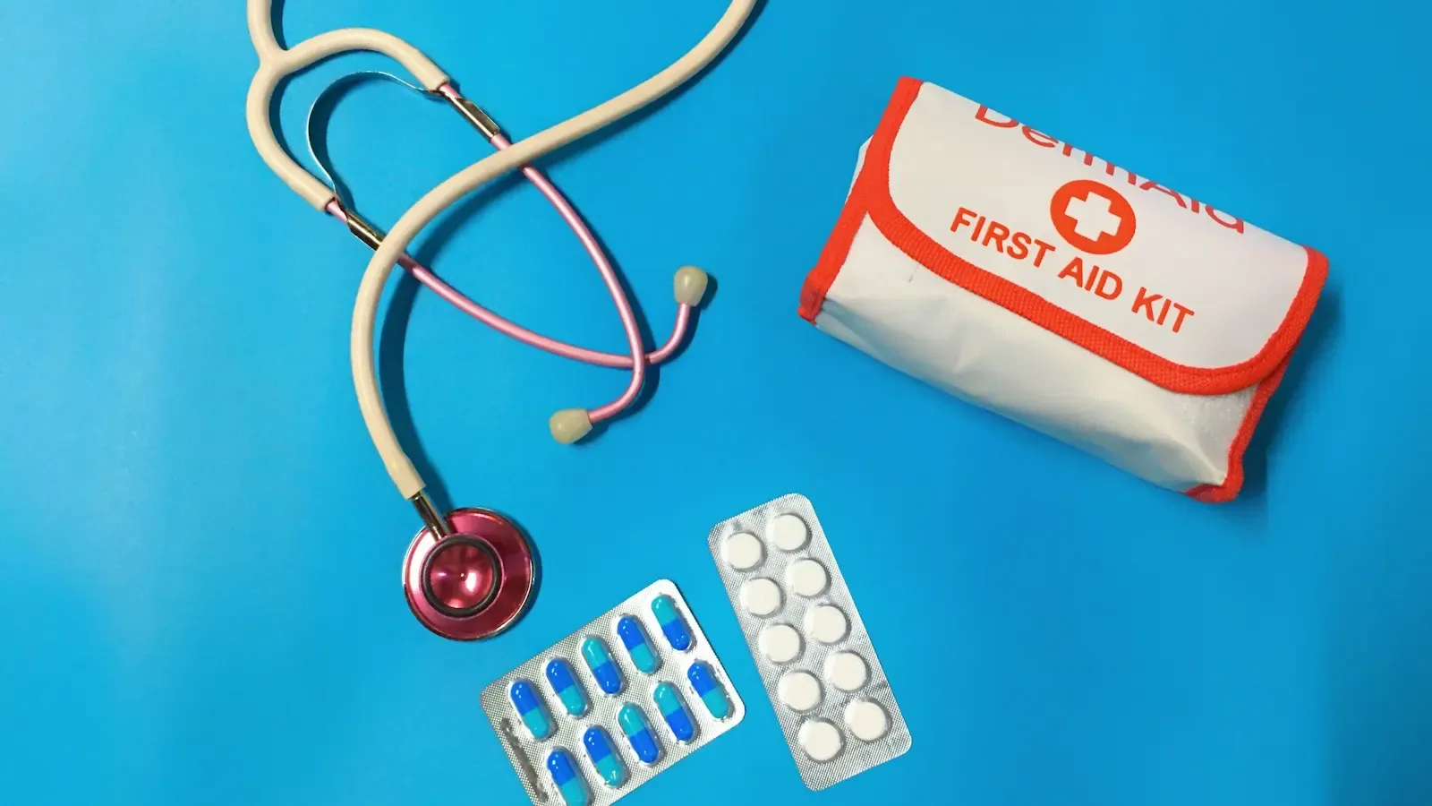 A stethoscope, blister packs of pills and a red-and-white first aid kit on a bright blue background