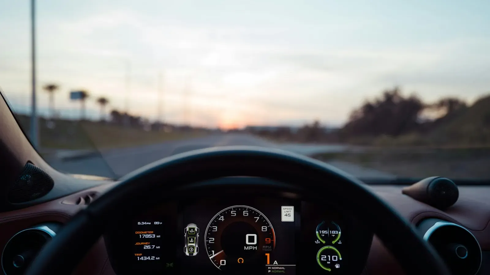 View from the driver's seat of a car on an open road at sunset, with the steering wheel and digital instrument cluster in the foreground