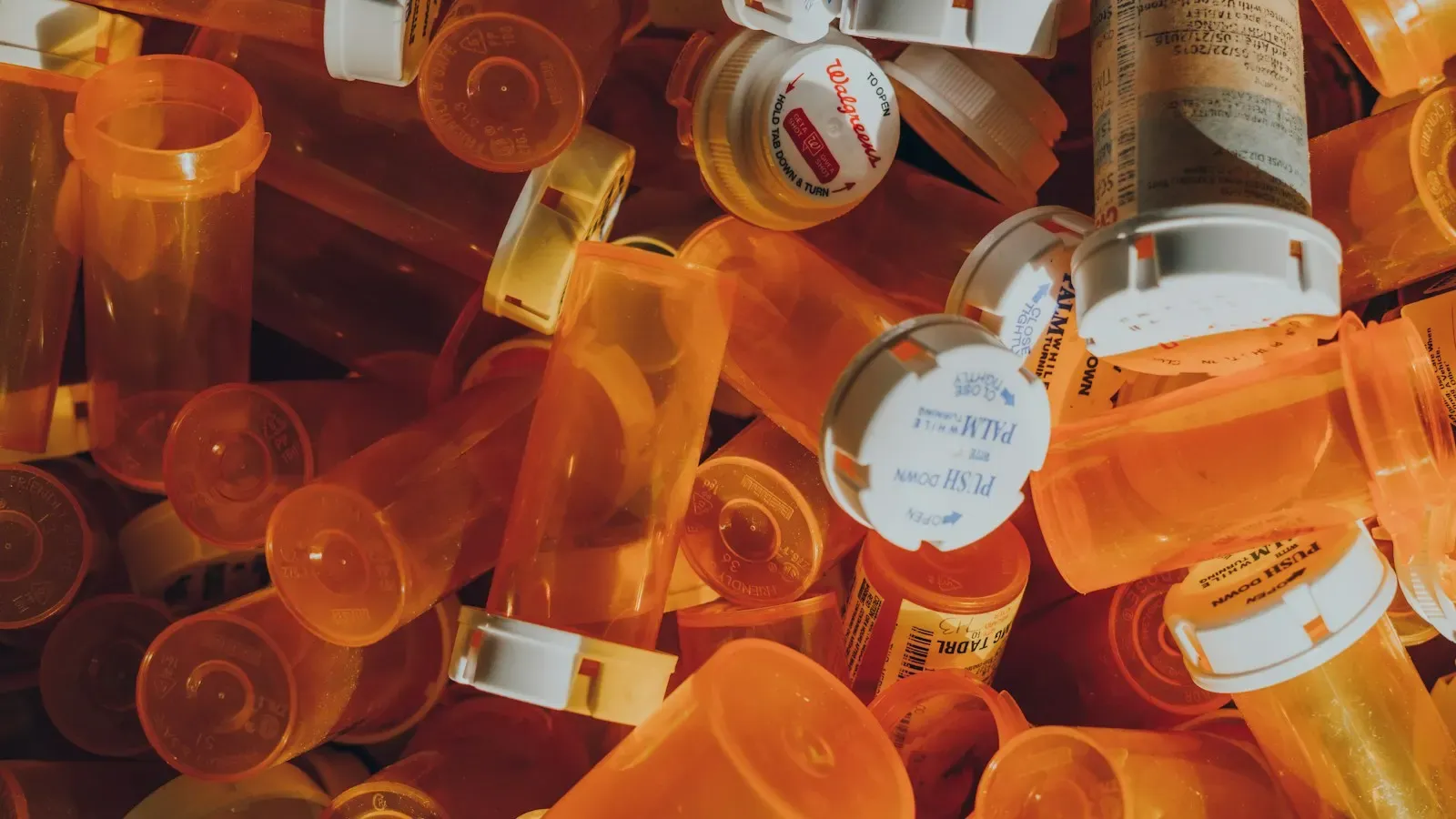 A pile of empty orange prescription pill bottles with white caps
