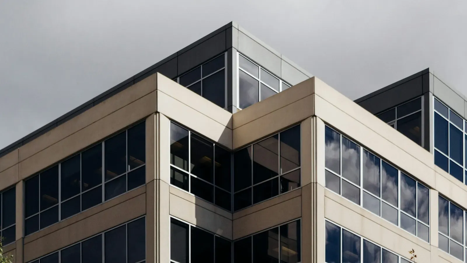 A modern white office building with dark glass windows under an overcast sky
