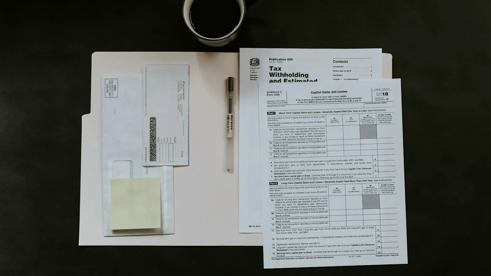 IRS tax forms, including a Tax Withholding and Estimated Tax publication, laid out on a dark desk next to a pen and a cup of coffee