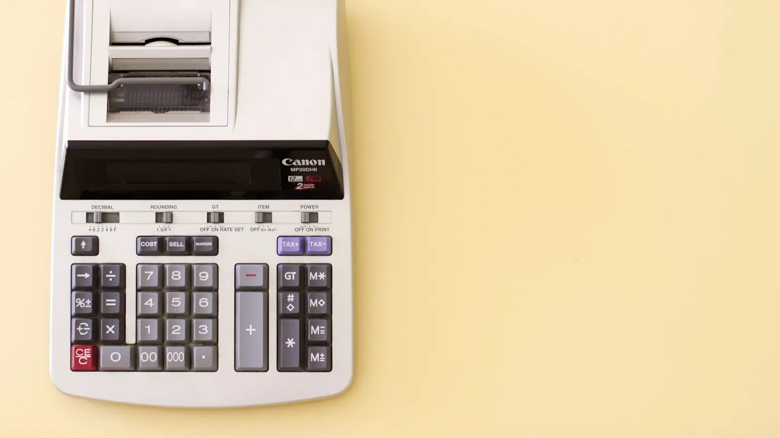 A printing desktop calculator with a paper roll on a pale yellow background