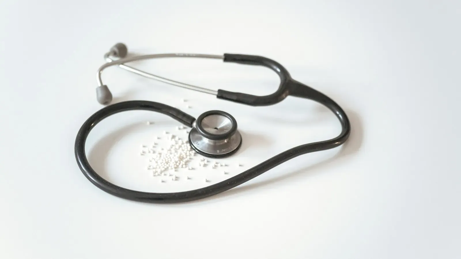 A black stethoscope with a silver chest piece lying on a plain white surface