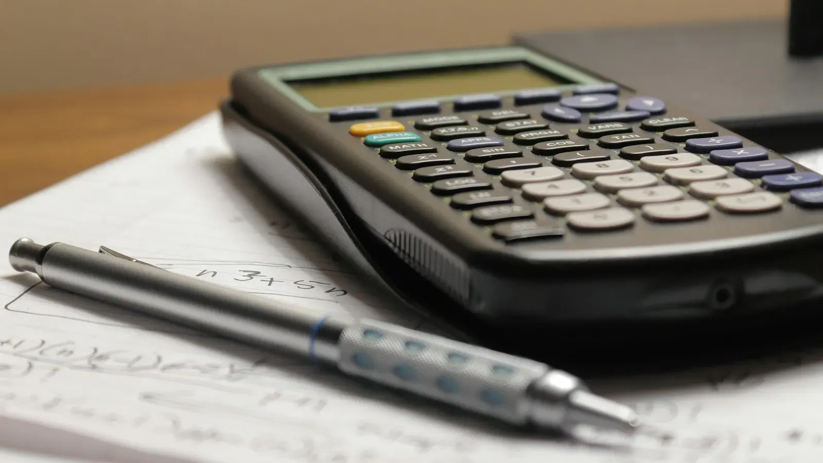 A black scientific calculator and a mechanical pencil resting on a sheet of handwritten calculations