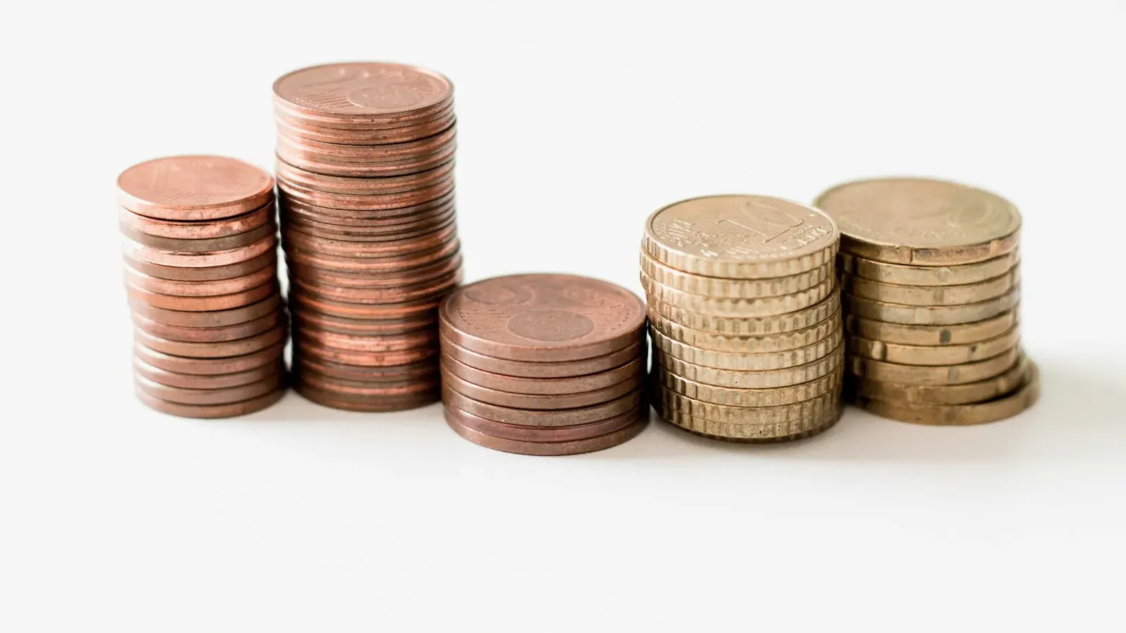 Five stacks of copper and gold-colored coins of increasing height on a white surface